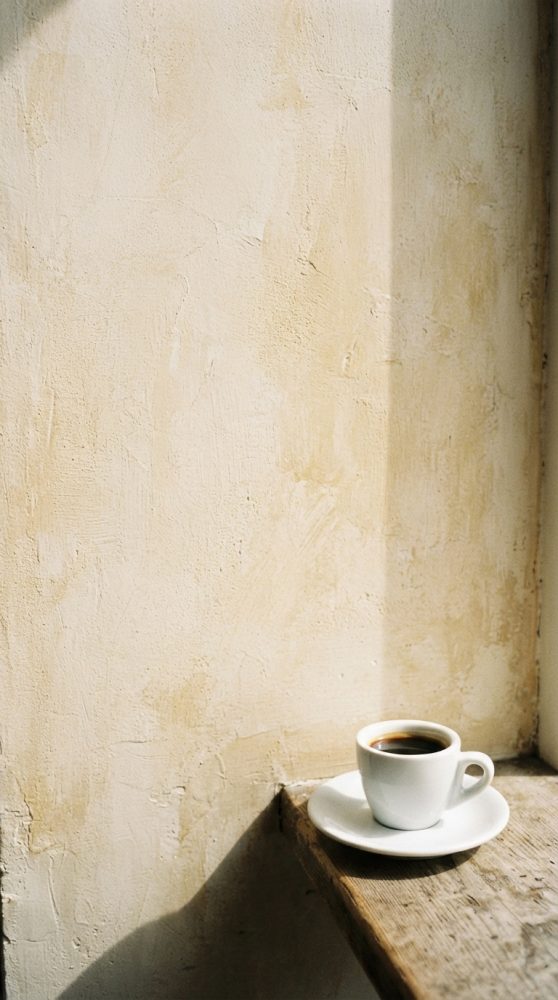 Chávena branca com café numa mesa de madeira rústica junto a parede bege clara com luz natural