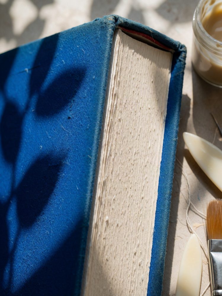 Livro antigo com capa azul e páginas envelhecidas ao lado de acessórios de restauro