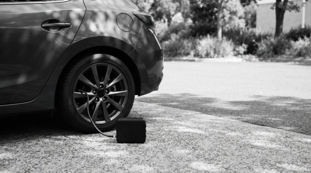 Compressor portátil conectado ao pneu traseiro de um carro estacionado em pavimento exterior