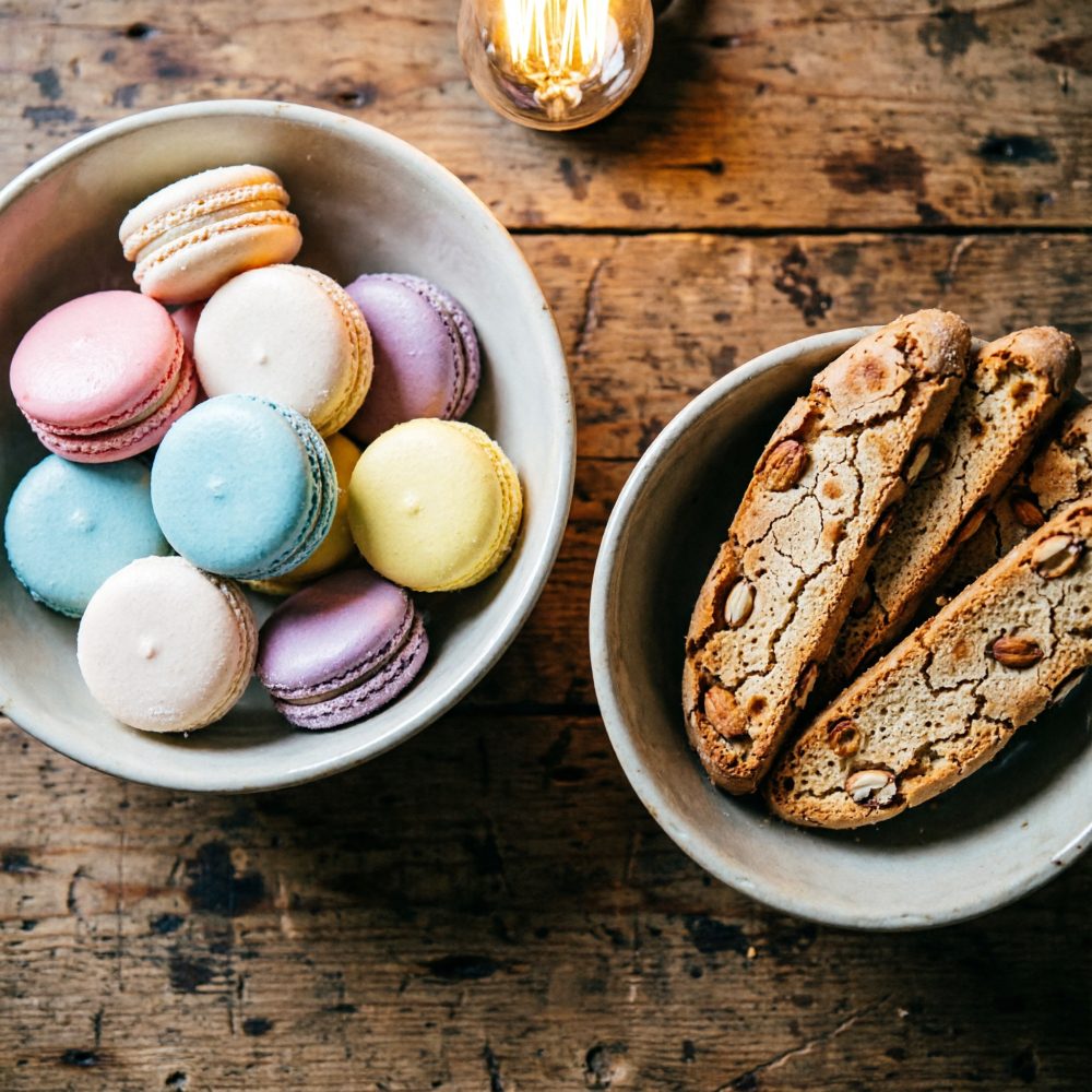 Taças com macarons coloridos e biscotti com amêndoas sobre mesa de madeira rústica