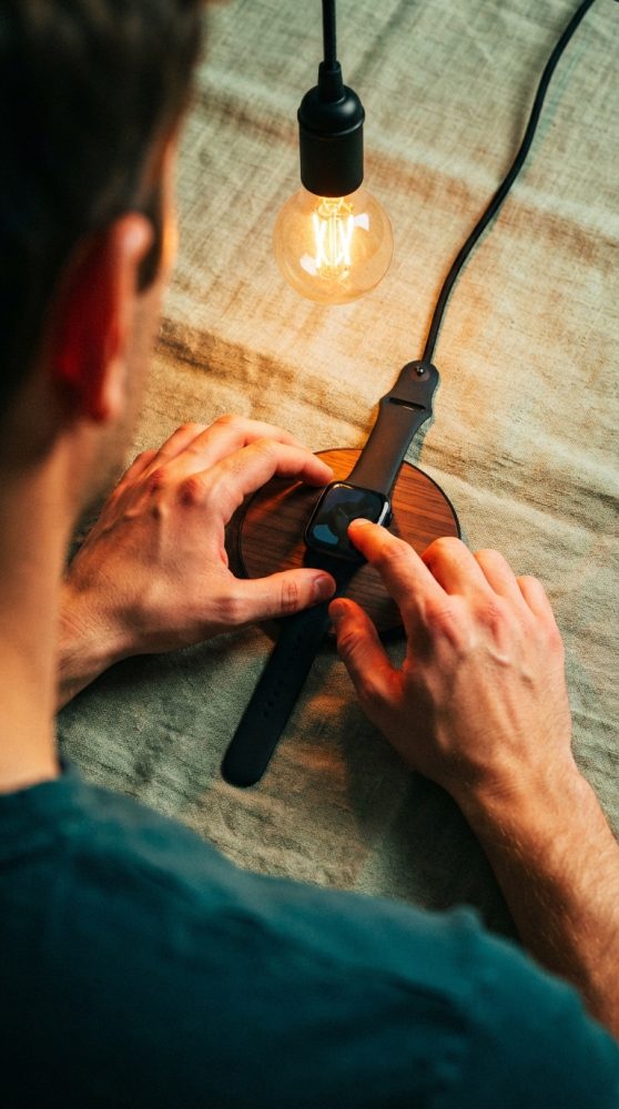 Homem a tocar num smartwatch preto sobre carregador wireless com lâmpada de filamento a iluminar