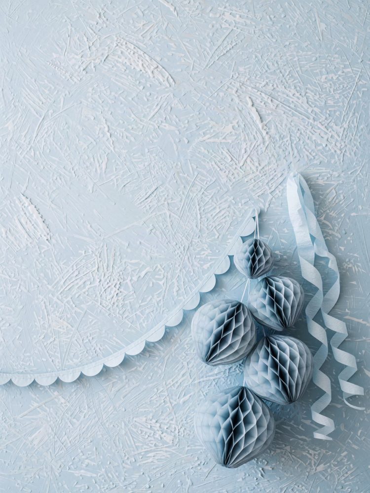 Bolas de papel azul penduradas e serpentinas brancas contra fundo azul texturizado
