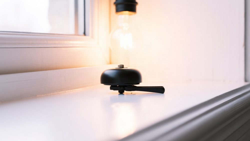 Campainha preta de bicicleta sobre superfície branca perto de janela com luz suave