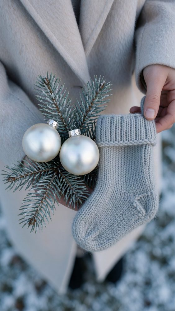 Pessoa segurando meia cinza em lã com ramos de pinheiro e bolas prateadas de Natal
