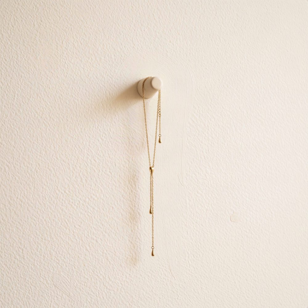 Colar dourado com pendentes finos pendurado numa peça branca contra parede creme texturada
