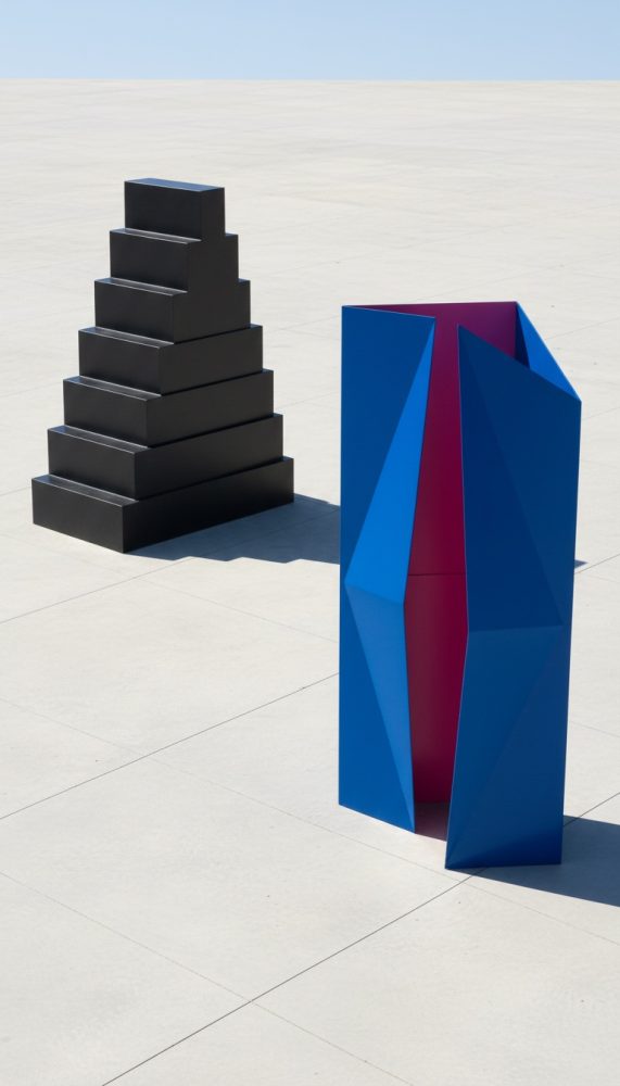 Esculturas geométricas abstratas preta em forma de escadaria e azul com interior vermelho em chão claro