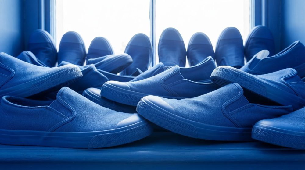 Múltiplas sapatilhas desportivas azuis simples tipo slip-on arrumadas por uma janela iluminada