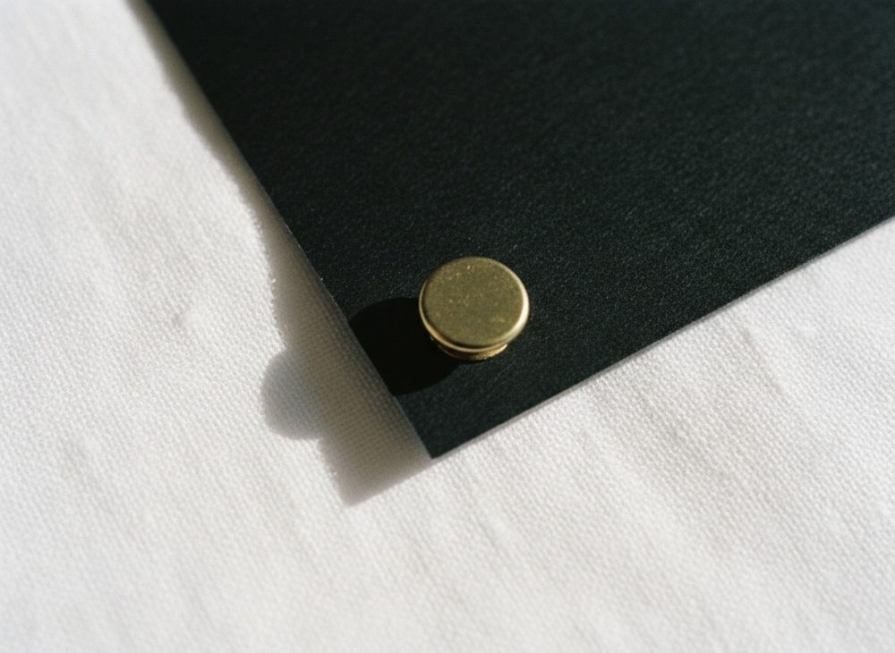 Alfinete dourado preso em canto de papel preto sobre mesa de tecido branco