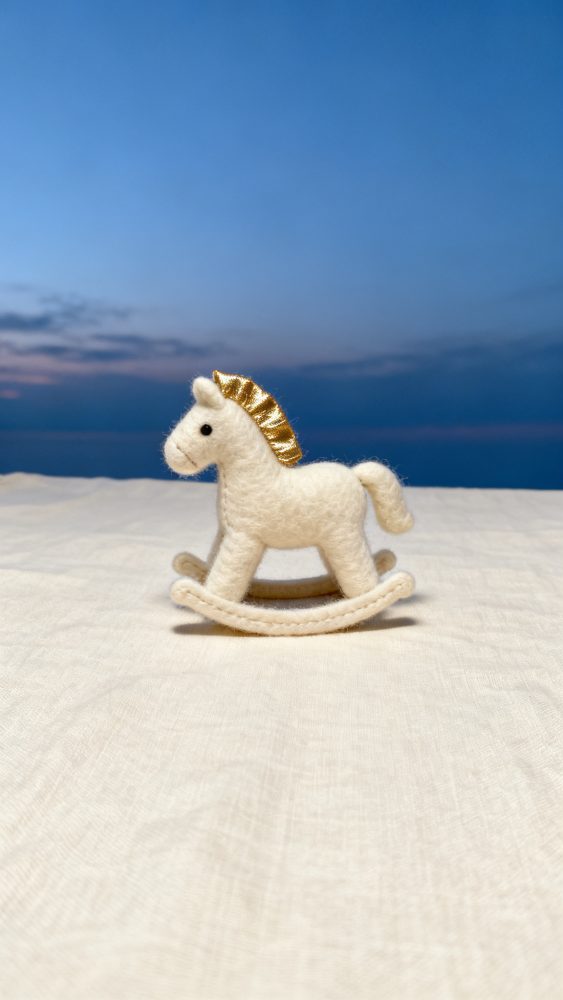 Brinquedo de cavalo de balanço branco em feltro com crina dourada sobre pano claro