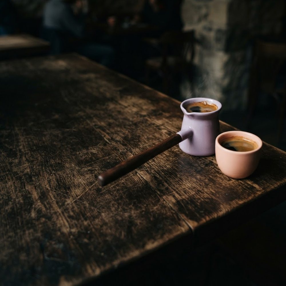 Cafeteira lilás e xícara pêssego com café quente a vapor sobre mesa de madeira rústica