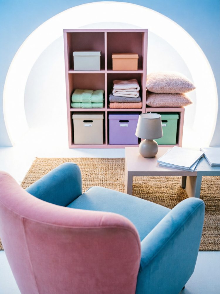 Estante com caixas coloridas, têxteis, poltrona bicolor e mesa com candeeiro sobre tapete de ráfia