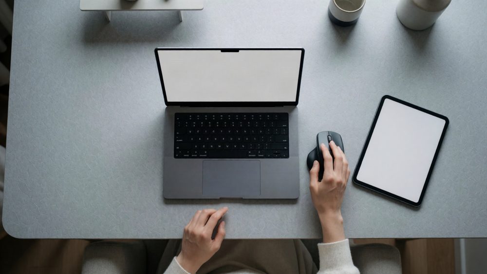 Mesa com portátil, tablet, rato e canecas numa disposição organizada vista de cima