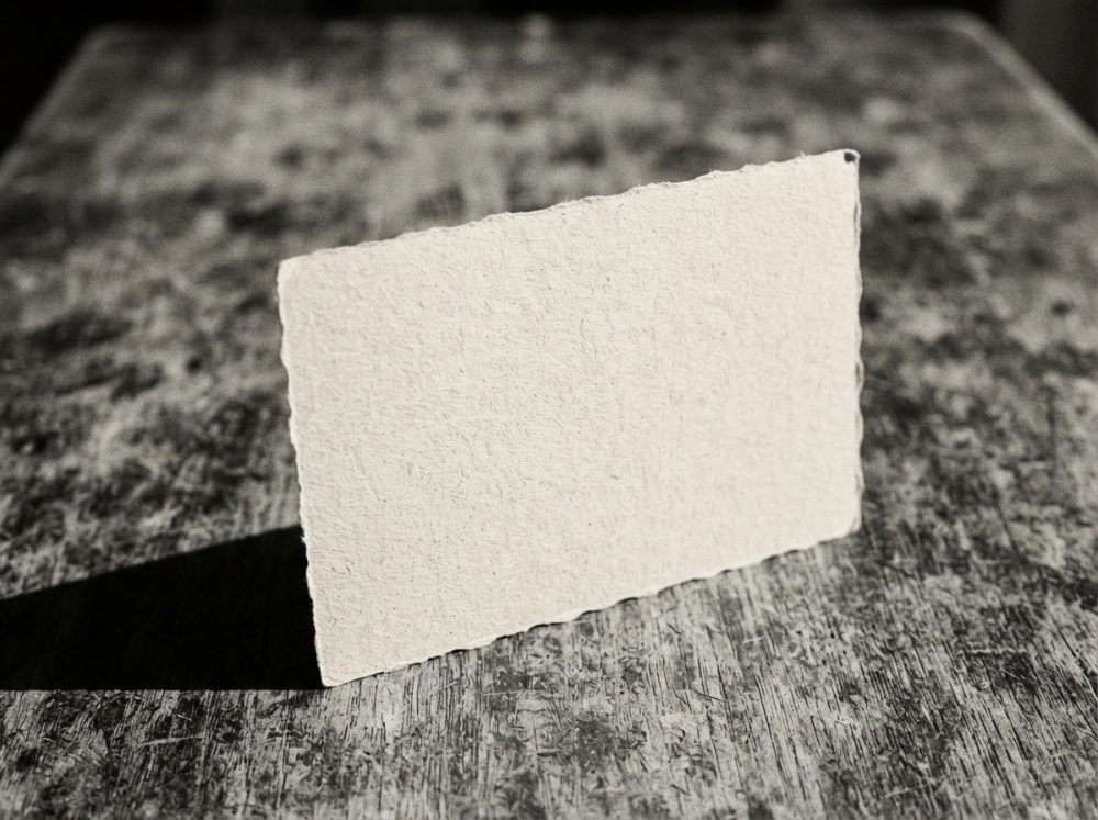Cartão branco de papel artesanal em pé sobre mesa de madeira com textura envelhecida