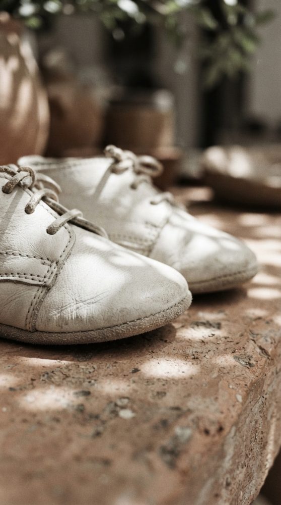 Sapatinhos de bebé em couro branco com atacadores numa superfície rústica com luz natural