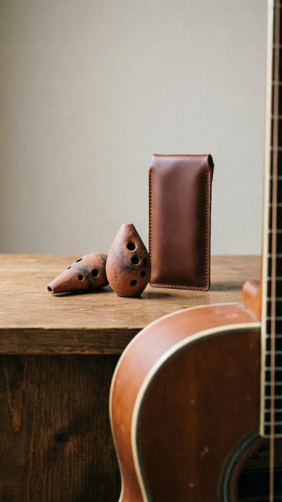 Duas ocarinas em cerâmica, estojo de couro castanho e parte de violão clássico numa mesa de madeira
