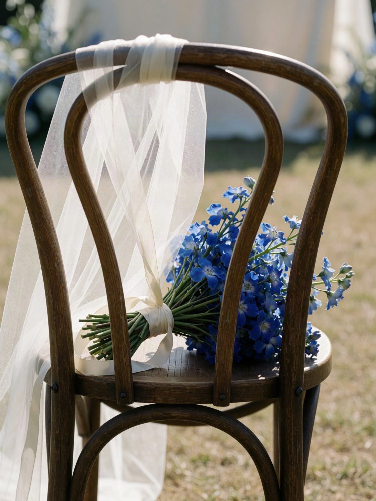 Cadeira de madeira com véu branco e bouquet de flores azuis para cerimónia de casamento ao ar livre