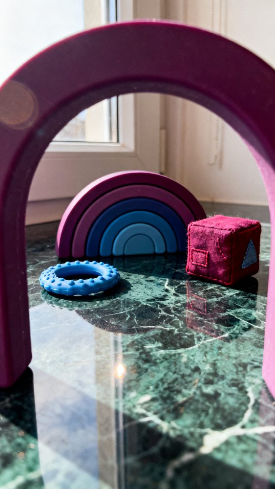 Brinquedos de bebé coloridos sobre mesa de mármore verde junto a janela com luz natural
