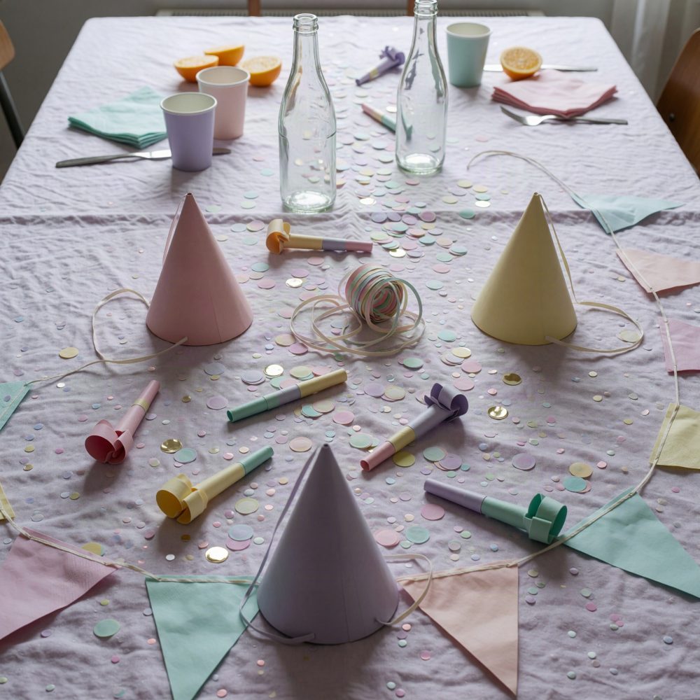 Mesa decorada com chapéus de festa, apitos, serpentinas, confetes e bandeirolas coloridas