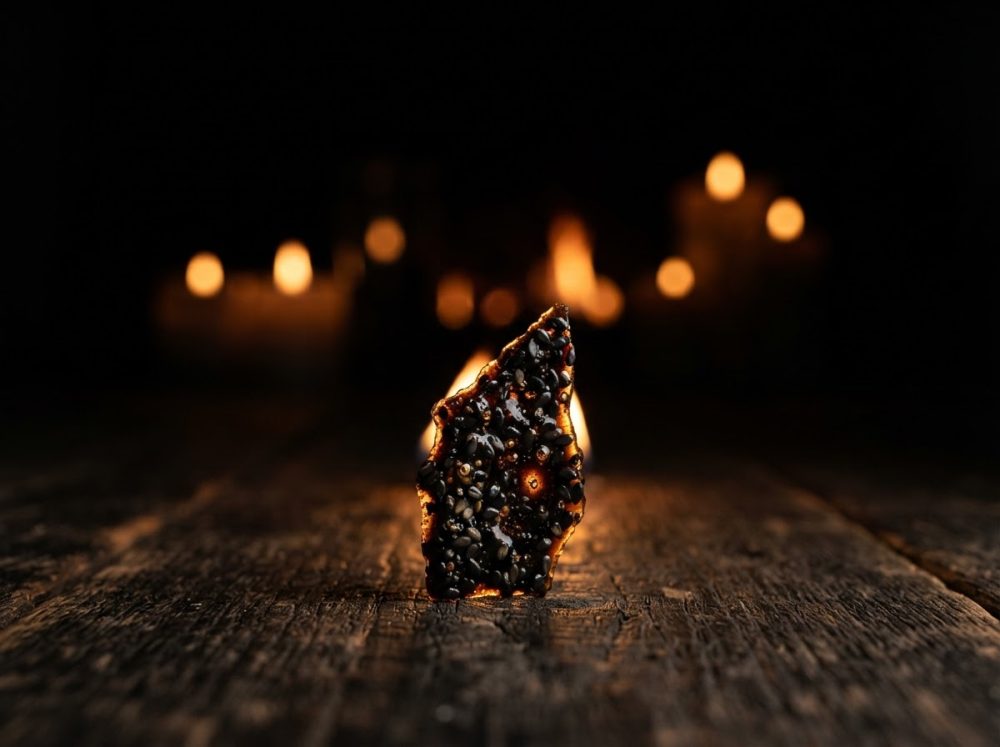 Peça de chocolate negro com sementes sobre mesa de madeira rústica iluminada por velas ao fundo