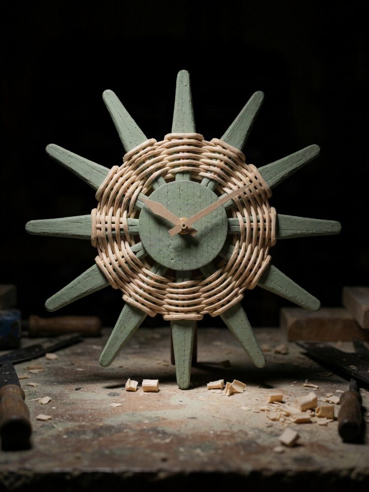 Relógio de parede em forma de sol feito de madeira verde e rattan sobre bancada de trabalho