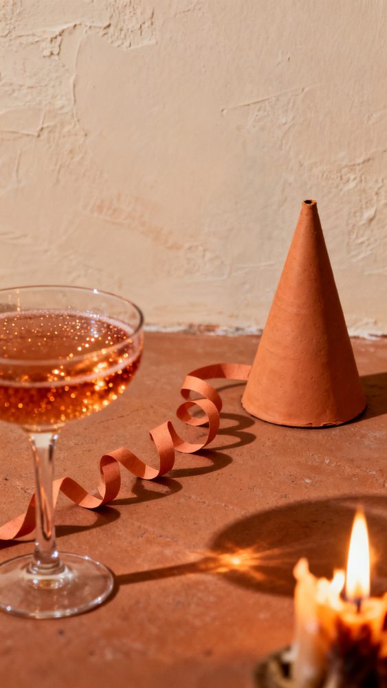 Taça de champanhe com fita e cone decorativo em terracota sobre mesa rústica com vela acesa