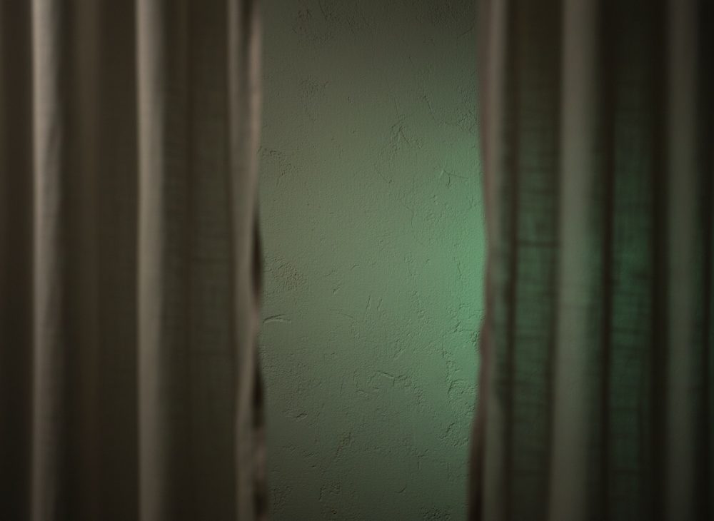 Parede verde texturada entre cortinas escuras parcialmente abertas com luz suave