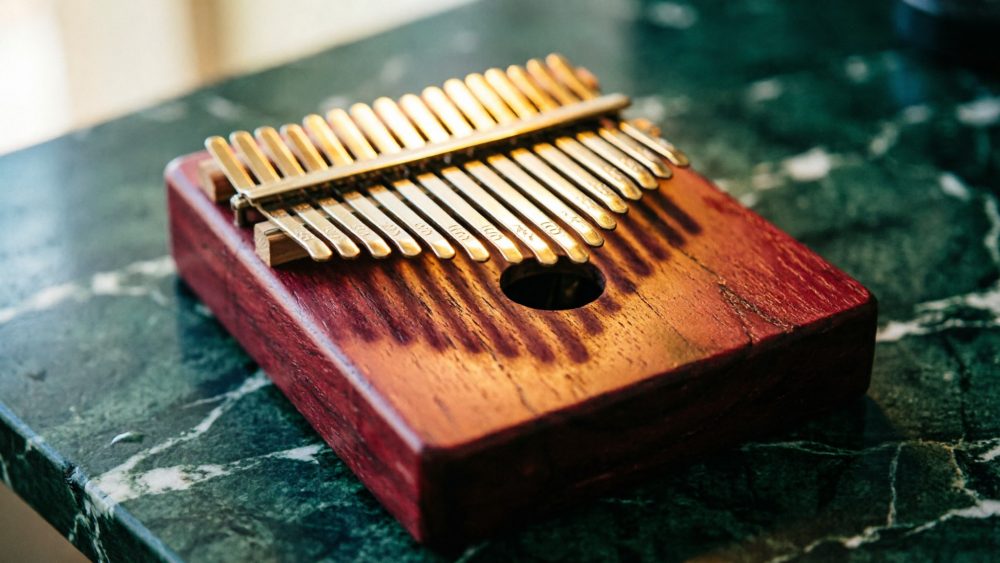 Instrumento kalimba de madeira castanha com teclas metálicas douradas em mesa de pedra verde