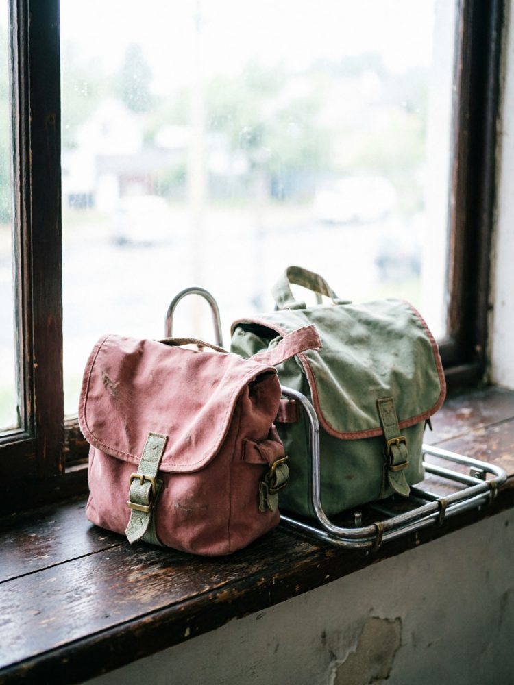 Duas bolsas para bicicleta em tecido rosa e verde sobre bagageira metálica junto a janela antiga