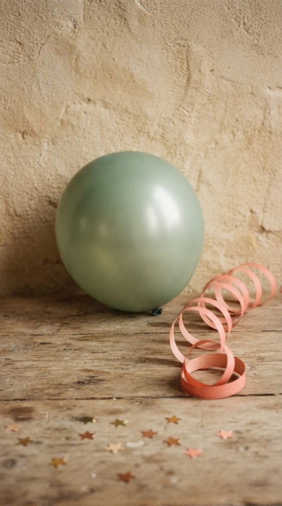 Balão verde com serpentina rosa e confetes dourados sobre mesa de madeira rústica