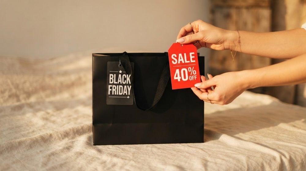 Saco preto com etiquetas Black Friday e desconto 40% segurada por mãos sobre tecido claro