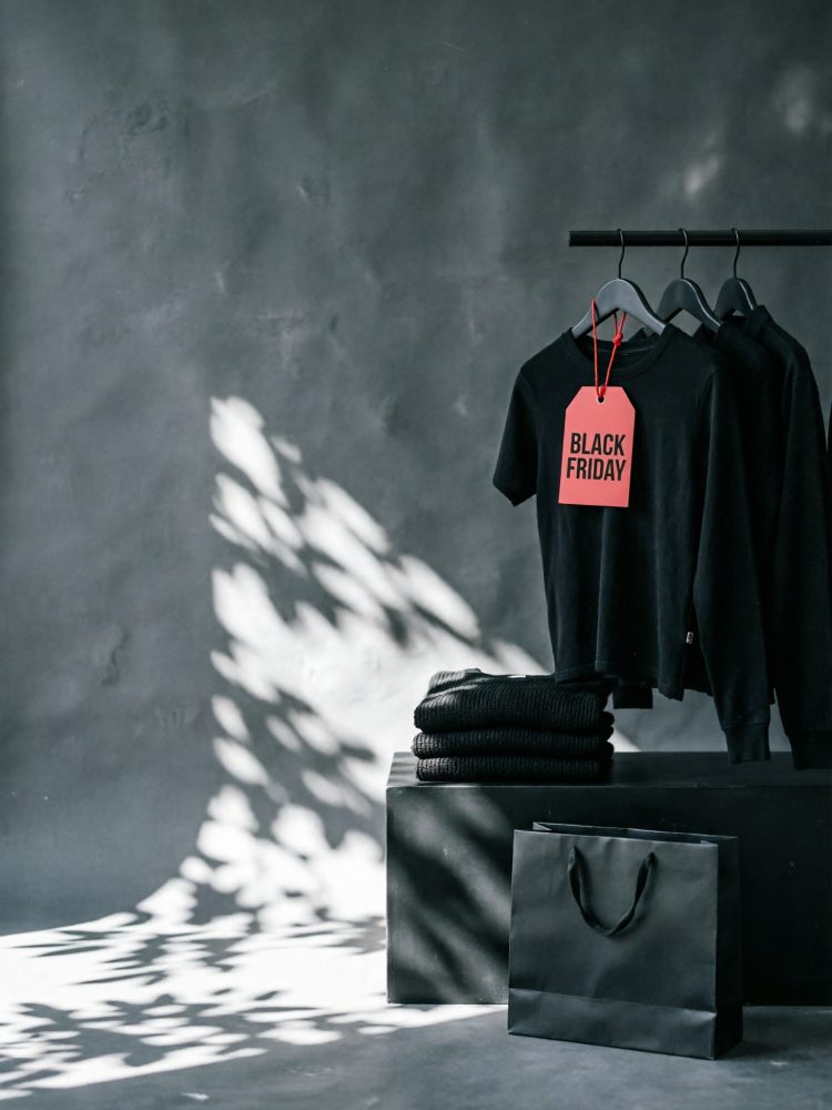 Camisola preta com etiqueta vermelha Black Friday e roupas empilhadas num fundo cinzento texturado
