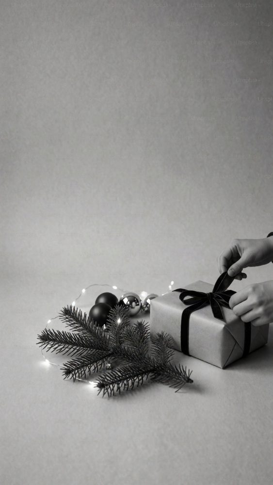 Mãos amarram laço preto num presente com enfeites de Natal e luzes