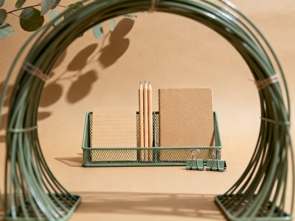 Organizador verde com lápis, bloco, caderno kraft e clipes em fundo castanho
