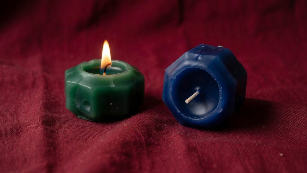 Velas verde acesa e azul apagada sobre tecido vermelho