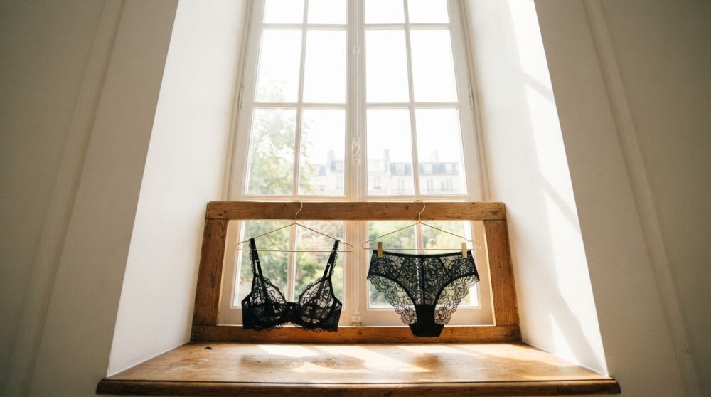 Conjunto de lingerie preta rendada pendurado em janela de madeira com luz natural
