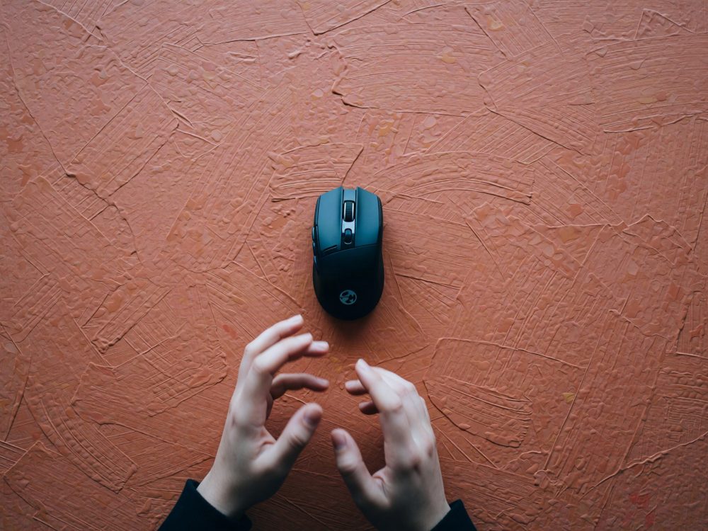 Rato de gaming preto sem fios com mãos sobre uma superfície castanha texturada