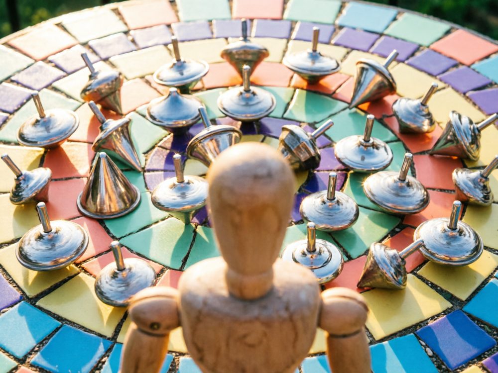 Pião metálico em mesa de mosaico colorido com manequim de madeira em primeiro plano