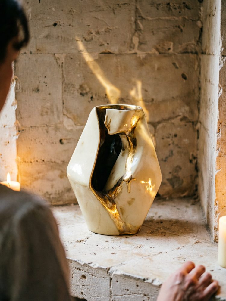 Vaso cerâmico abstrato branco com detalhes dourados sobre superfície de pedra rústica iluminada