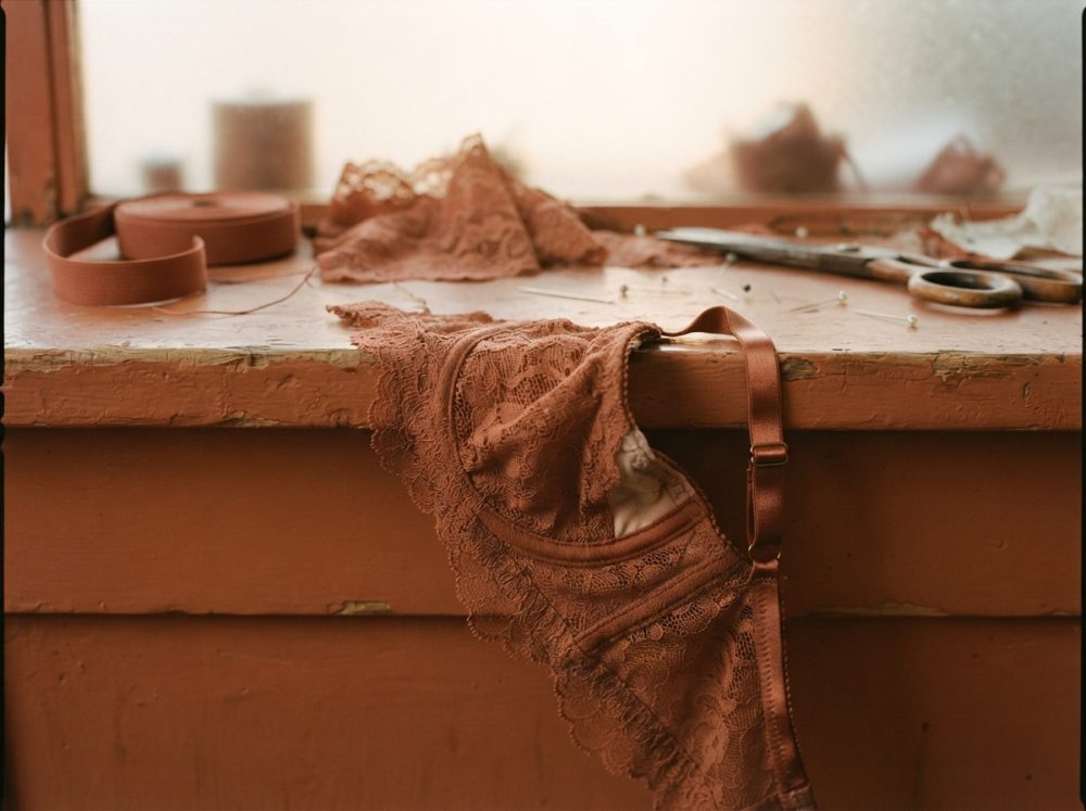 Conjunto de lingerie de renda castanha sobre tampo de madeira com acessórios de costura