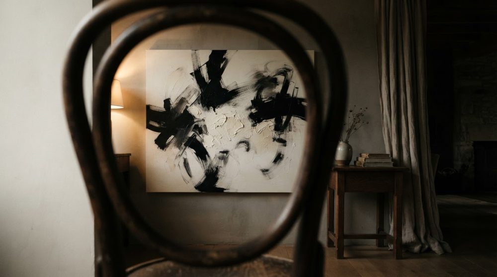 Cadeira em madeira a enquadrar quadro abstrato preto e branco numa sala com luz suave