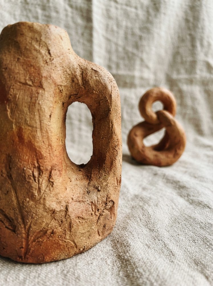 Esculturas abstratas em terracota com textura rústica sobre tecido cinza