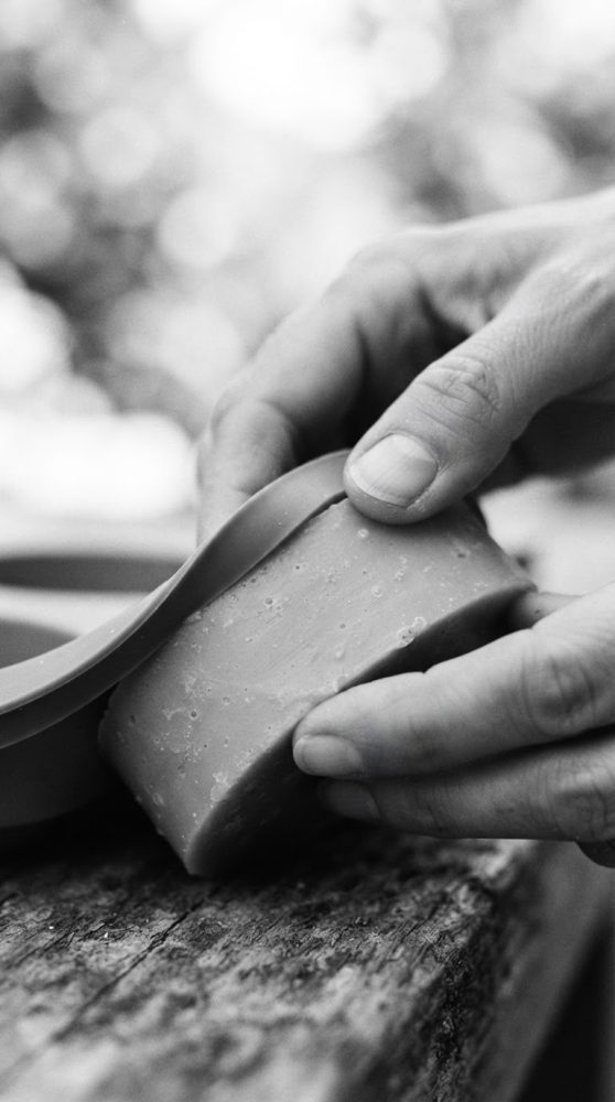Mãos a desenformar barra de sabão artesanal de molde de silicone sobre madeira rústica