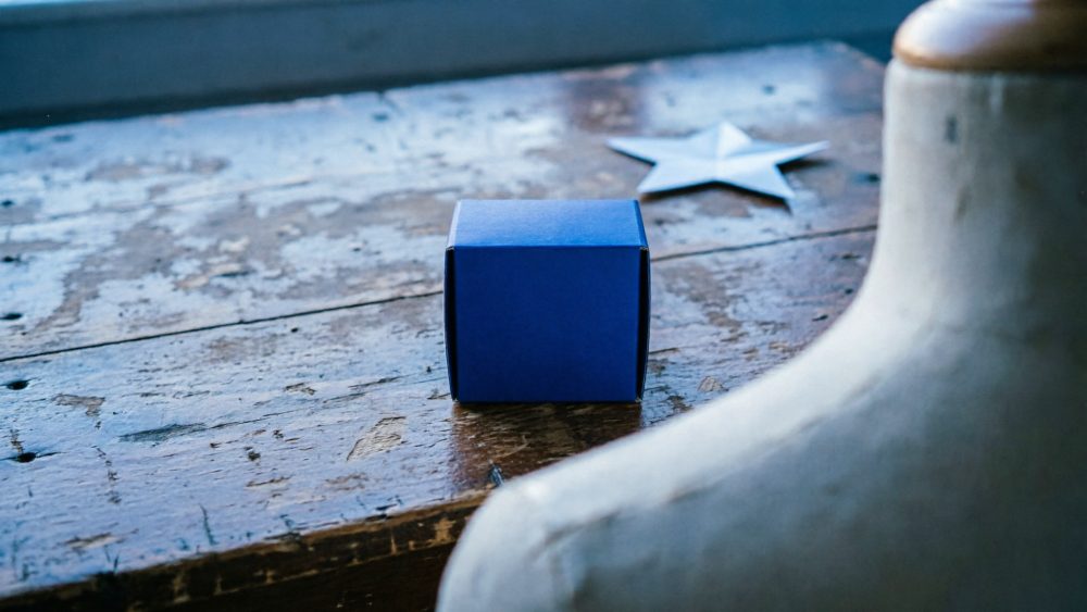 Caixa azul pequena sobre mesa de madeira rústica com estrela metálica desfocada ao fundo