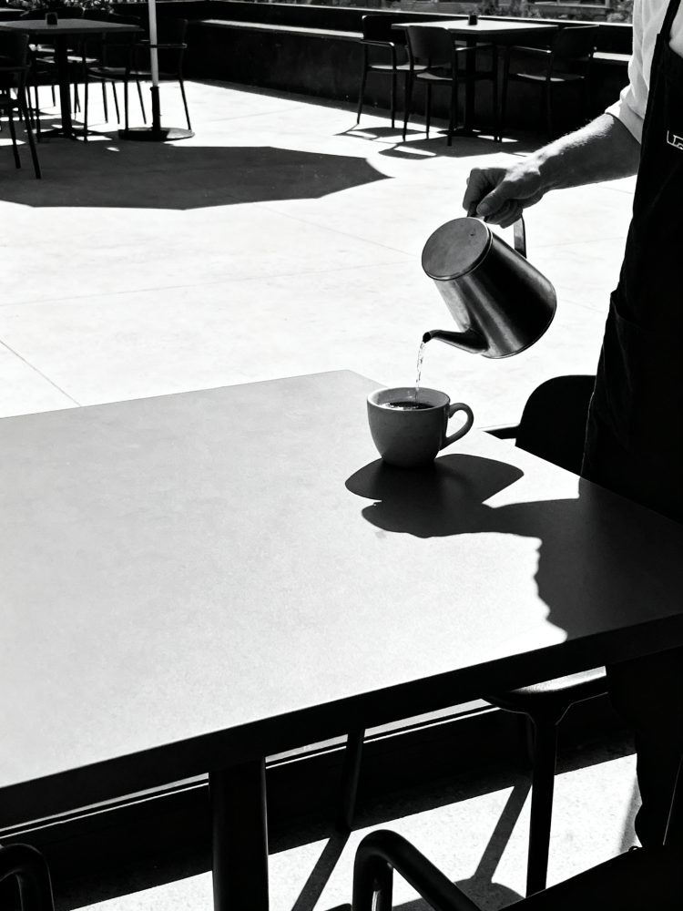 Pessoa a servir café numa chávena numa mesa numa esplanada com luz e sombra fortes