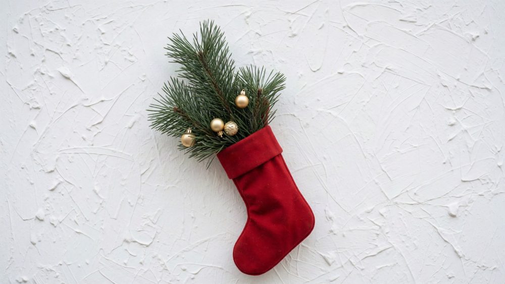 Meia vermelha de Natal com ramos de pinheiro e bolas douradas num fundo branco texturado