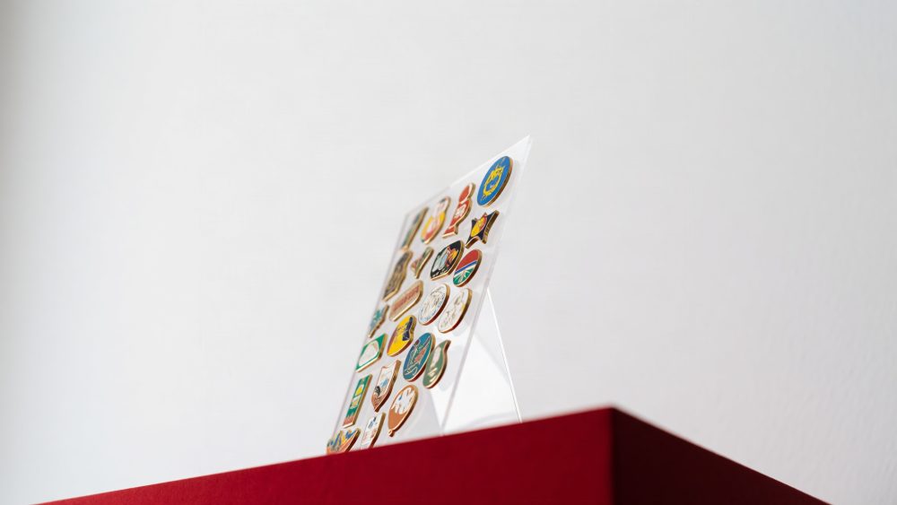 Expositor transparente com pins coloridos sobre superfície vermelha em fundo branco