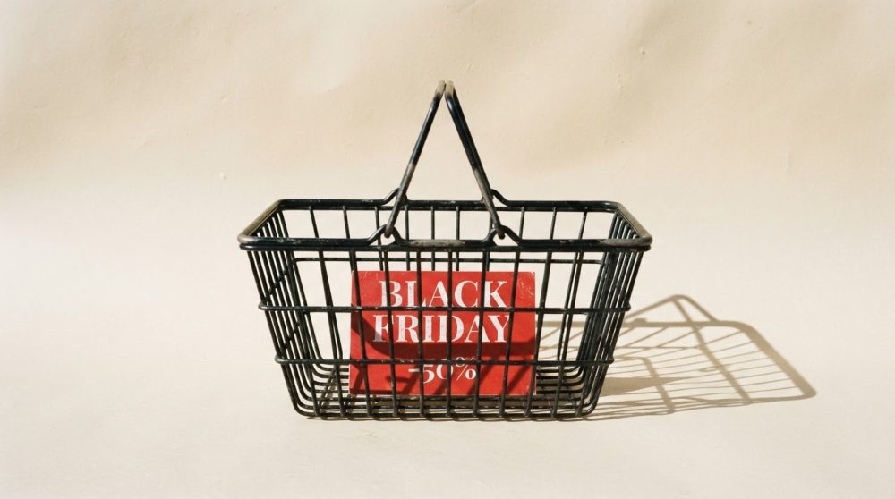Cesta preta de compras com placa vermelha a indicar 50% desconto Black Friday sobre fundo claro