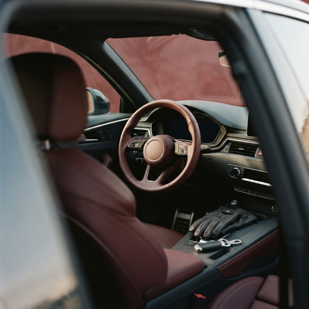 Interior de carro com volante em couro castanho, assentos em couro e luvas com chave no apoio central