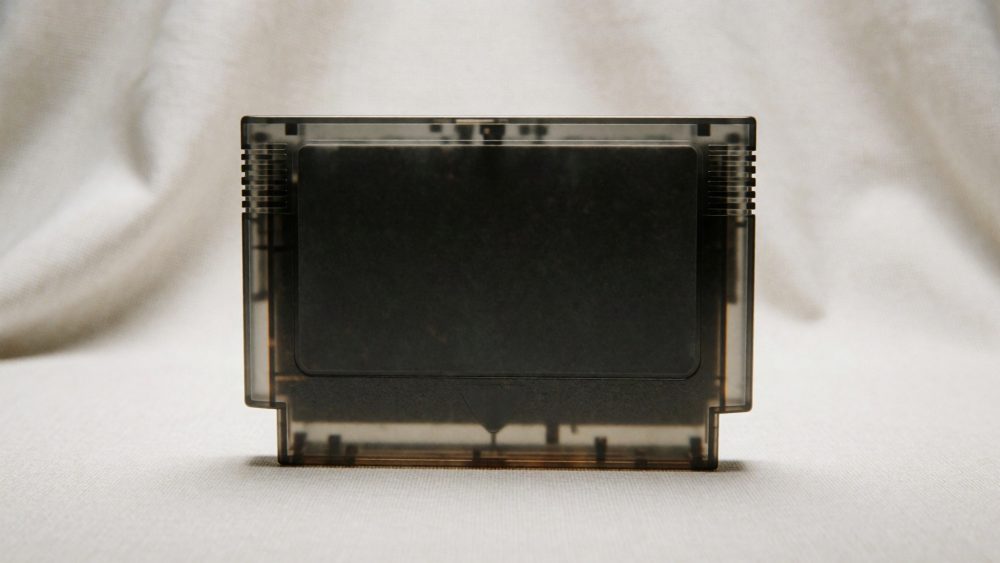 Cartucho de videojogo retro com caixa plástica transparente escura sobre fundo claro
