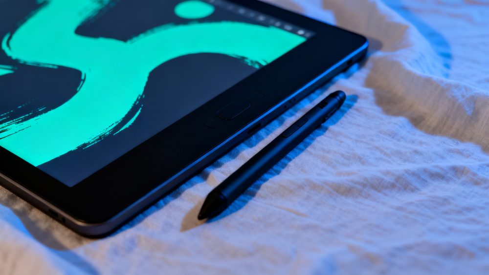 Tablet com ecrã iluminado e caneta digital sobre superfície clara texturada
